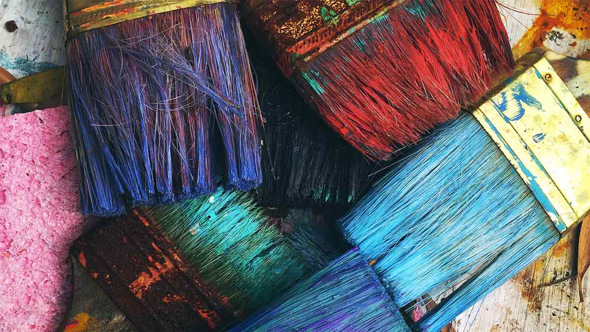 Photo de pinceaux de peinture posés les uns sur les autres, avec plusieurs couleurs : bleu, rouge, violet, noir et vert.